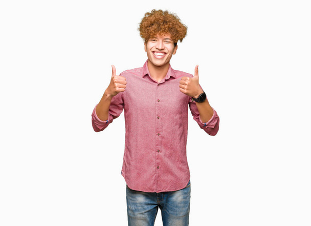Young handsome business man with afro hair success sign doing positive gesture with hand, thumbs up smiling and happy. Looking at the camera with cheerful expression, winner gesture. - Fotografie, Obrázek