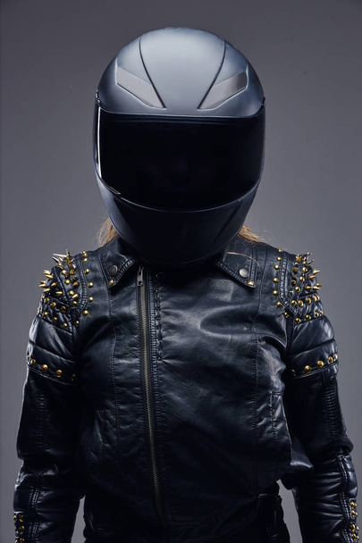 Мода, спорт, экстрим. Портрет байкерши в костюме гонщика и защитном шлеме в студии на сером фоне
. - Фото, изображение