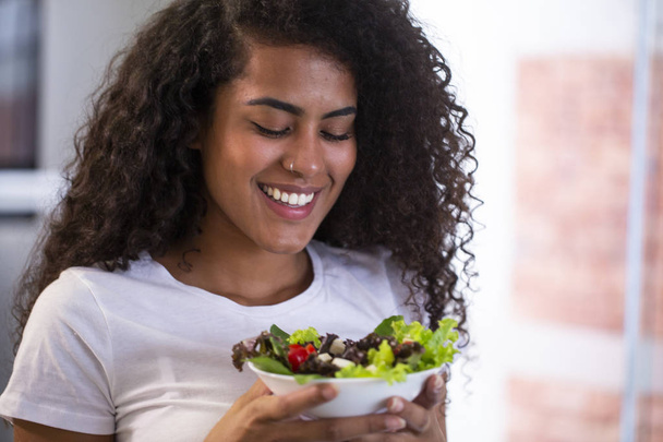 gai jeune afro américaine femme manger salade de légumes dans la cuisine à la maison
. - Photo, image