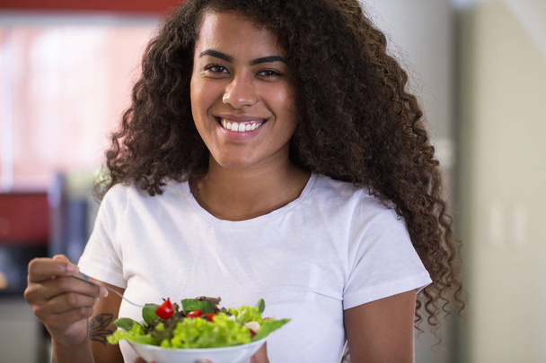 joyeuse jeune femme afro-américaine manger salade de légumes dans la cuisine à la maison - Imagem
. - Photo, image