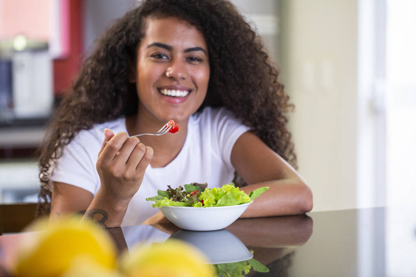 cheerful young afro american woman eating vegetable salad in home kitchen - Imagem. - Photo, Image