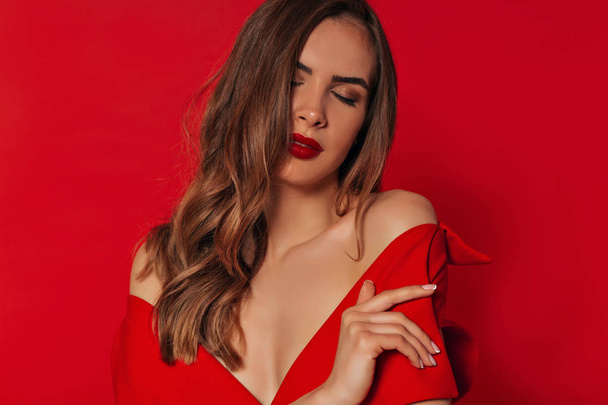 Tederheid romantisch glanzende stijlvolle vrouw met golvend goud haar en heldere make-up dragen rode jurk met blote schouders  - Foto, afbeelding