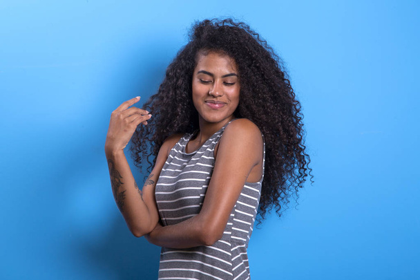 Portré a mosolygó fekete nő afro frizurát a kék háttér-imagem. - Fotó, kép