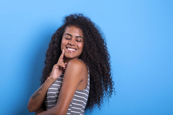 Portrait of smiling black woman with afro hairstyle on blue background - Imagem. - Fotó, kép