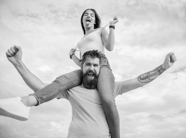 There is chemistry between them. Bearded man piggybacking his girlfriend just for fun. Hipster giving sexy woman a piggyback ride. Happy couple in love on cloudy sky. Loving couple smile having fun - Foto, afbeelding