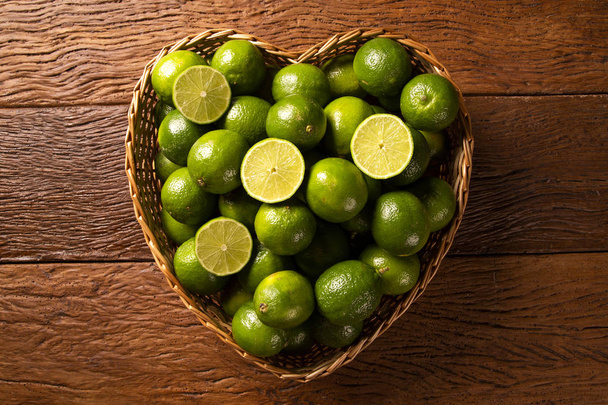 Fresh limes in a heart bowl on wooden table background. Top view - Photo, Image