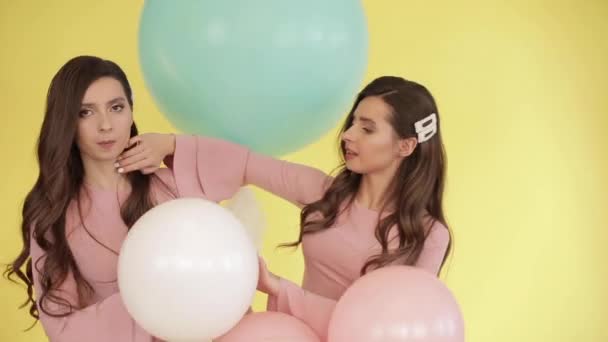 Hübsche Zwillinge in rosa Kleidern spielen mit bunten Luftballons - Filmmaterial, Video