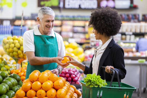 African Customer with greengrocer, holding orange fruit. - Foto, imagen