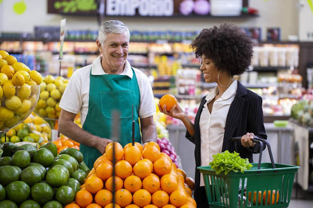 African Customer with greengrocer, holding orange fruit. - Foto, Imagen
