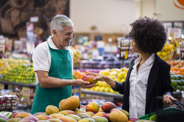 African Customer with greengrocer, holding mango. - Fotoğraf, Görsel