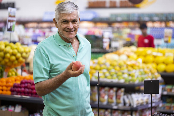 Handsome man posing, looking and holding fruit in hand. Bearded customer smiling. Section with fresh citruses on background. - Foto, Imagem