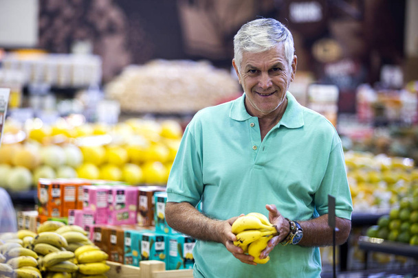 Handsome man posing, looking at camera and holding melon in hand. Bearded customer smiling. Section with fresh citruses on background. - Φωτογραφία, εικόνα
