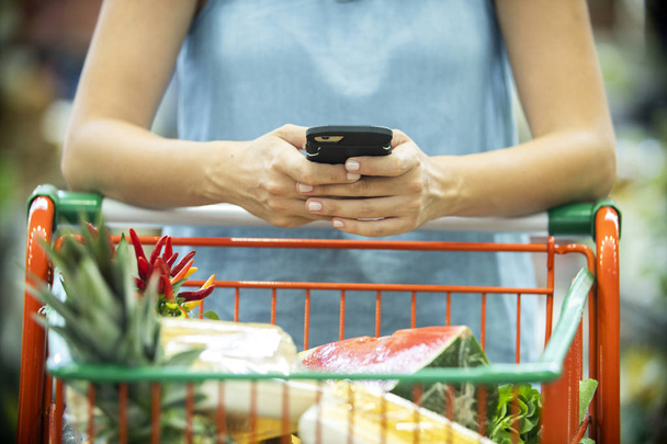 Woman using mobile phone while shopping in supermarket - Foto, Imagen