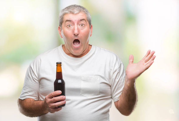 Przystojny mężczyzna senior picia butelka piwa na na białym tle bardzo szczęśliwy i podekscytowany, zwycięzca wyrażenie świętuje zwycięstwo krzyczy z uśmiechem i podniósł ręce - Zdjęcie, obraz
