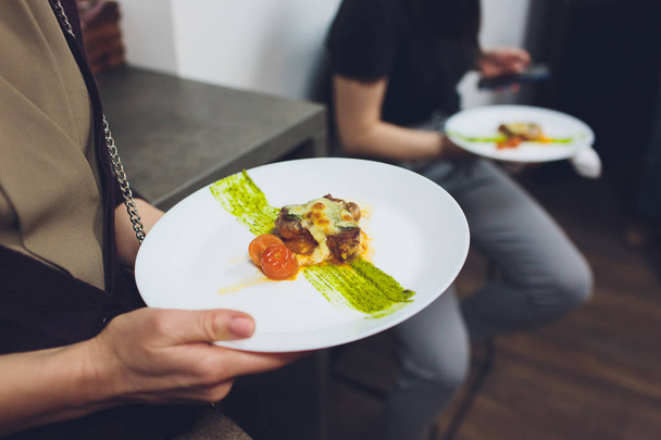 Uroskokki koristelee salaattiastiaa ravintolan keittiössä mustassa esiliinassa. lähikuva kädestä pihdeillä
. - Valokuva, kuva