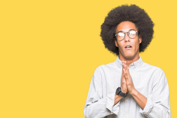 Americký mladík s afro vlasy nosí brýle prosit a modlit se s rukama naděje výraz na tváři velmi emocionální a strach. Žádá o odpuštění. Pojem náboženství. - Fotografie, Obrázek