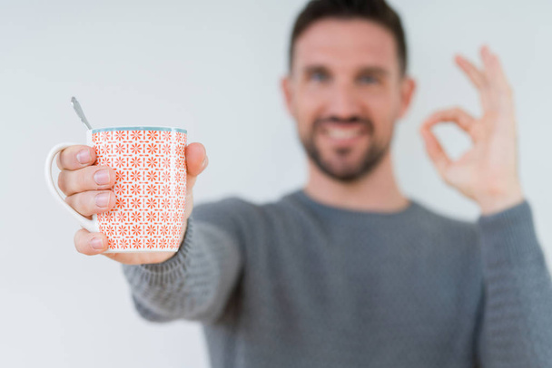 Fiatalember driking csésze kávé felett elszigetelt háttér csinál rendben jel ujjakkal, kiváló szimbólum - Fotó, kép