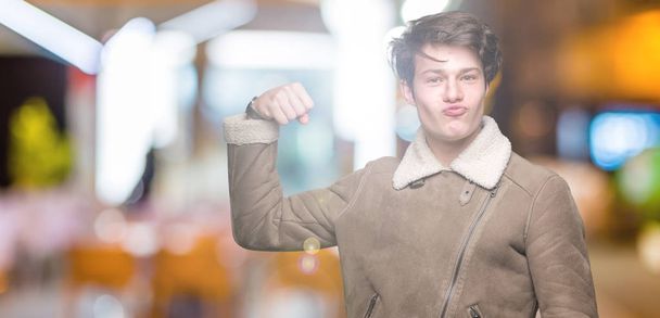Όμορφος νεαρός φορώντας παλτό χειμώνα πάνω από απομονωμένες φόντο ισχυρή πρόσωπο δείχνει μυ των βραχιόνων, αυτοπεποίθηση και υπερήφανοι της εξουσίας - Φωτογραφία, εικόνα