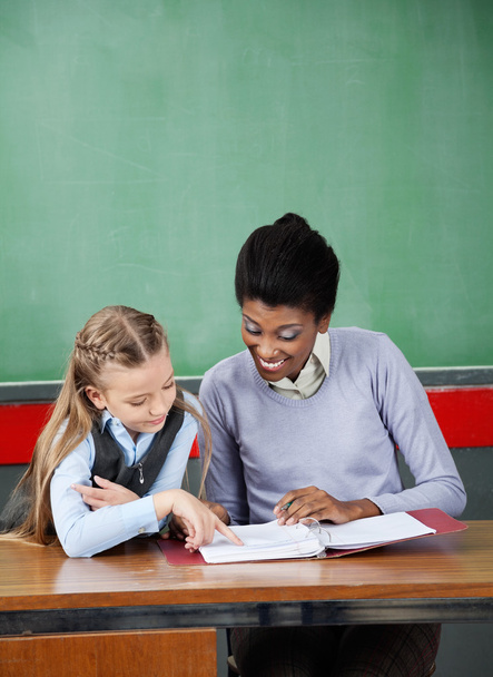 Schoolgirl Pointing In Binder With Teacher At Desk - Foto, afbeelding