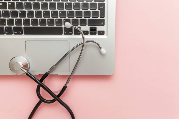 Stethoskop-Tastatur-Laptop isoliert auf rosa Hintergrund. moderne medizinische Informationstechnologie und Softwareentwicklung. Computer und Gadget Diagnose und Reparatur - Foto, Bild