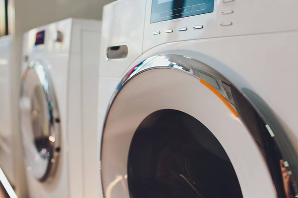 A row of industrial washing machines in a public laundromat. - 写真・画像