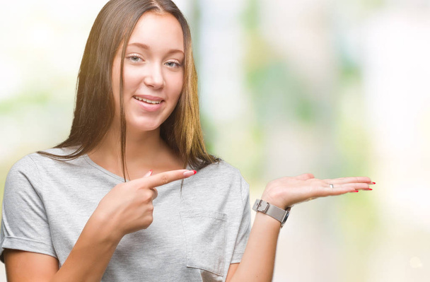 Young caucasian beautiful woman over isolated background amazed and smiling to the camera while presenting with hand and pointing with finger. - Φωτογραφία, εικόνα