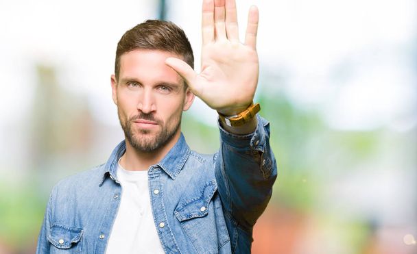 Handsome man with blue eyes and beard wearing denim jacket doing stop sing with palm of the hand. Warning expression with negative and serious gesture on the face. - Foto, Imagem