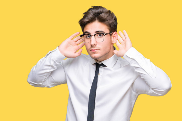 Молодой бизнесмен в очках на изолированном фоне пытается услышать жесты обеих рук, любопытные для сплетен. Проблемы со слухом, глухой
 - Фото, изображение