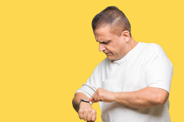 Мужчина средних лет в белой футболке на изолированном фоне Проверяет время на наручных часах, расслабленный и уверенный в себе
 - Фото, изображение