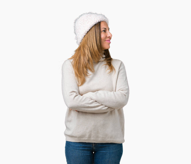 Mulher de meia-idade bonita vestindo suéter de inverno e chapéu sobre fundo isolado sorrindo olhando para o lado com os braços cruzados convencido e confiante
 - Foto, Imagem