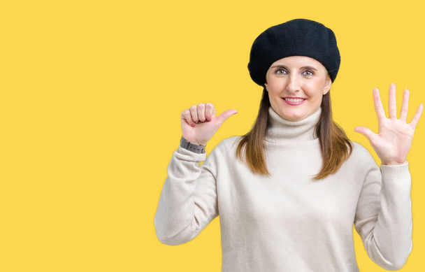 Middelbare leeftijd volwassen vrouw dragen winter trui en baret op geïsoleerde achtergrond weergeven en met de vingers omhoog nummer zes terwijl lacht zelfverzekerd en blij. - Foto, afbeelding