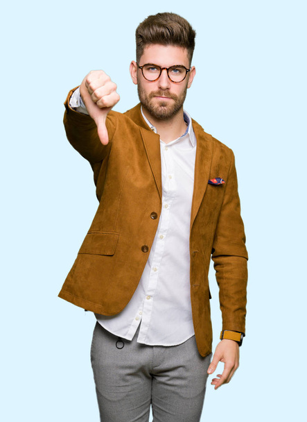 Young handsome business man wearing glasses looking unhappy and angry showing rejection and negative with thumbs down gesture. Bad expression. - Foto, Imagen