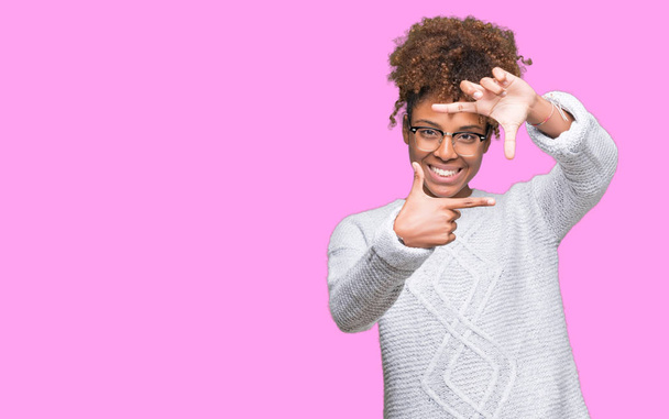 Mooie jonge african american vrouw winter trui dragen over geïsoleerde achtergrond glimlachend maken frame met handen en vingers met blij gezicht. Creativiteit en fotografie concept. - Foto, afbeelding