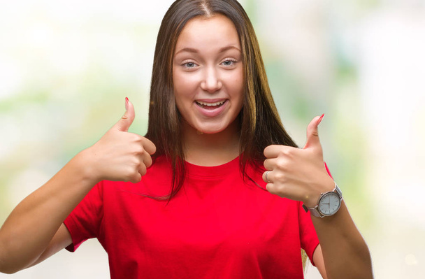 Young beautiful caucasian woman over isolated background success sign doing positive gesture with hand, thumbs up smiling and happy. Looking at the camera with cheerful expression, winner gesture. - Photo, Image