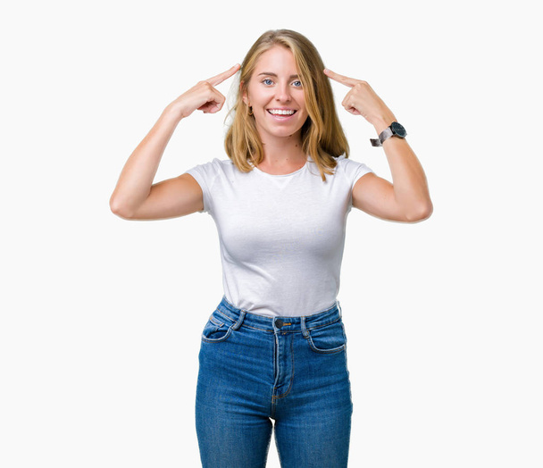 Mooie jonge vrouw dragen casual wit t-shirt over geïsoleerd background Smiling wijzend naar hoofd met beide handen vinger, geweldig idee of gedachte, goed geheugen - Foto, afbeelding