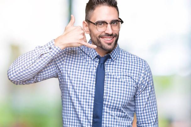 Joven hombre de negocios con gafas sobre un fondo aislado sonriendo haciendo un gesto telefónico con la mano y los dedos como hablando por teléfono. Comunicar conceptos
. - Foto, imagen