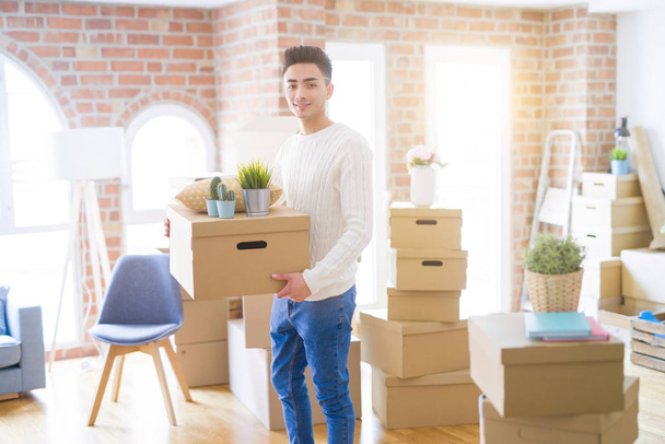 Jonge man glimlachend holdig kartonnen doos, gelukkig verhuizen naar een nieuwe Ho - Foto, afbeelding