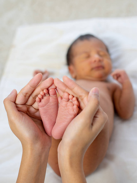 Mother hands hold little newborn baby feet with love emotion and the baby is sleeping on white bed - Foto, Bild