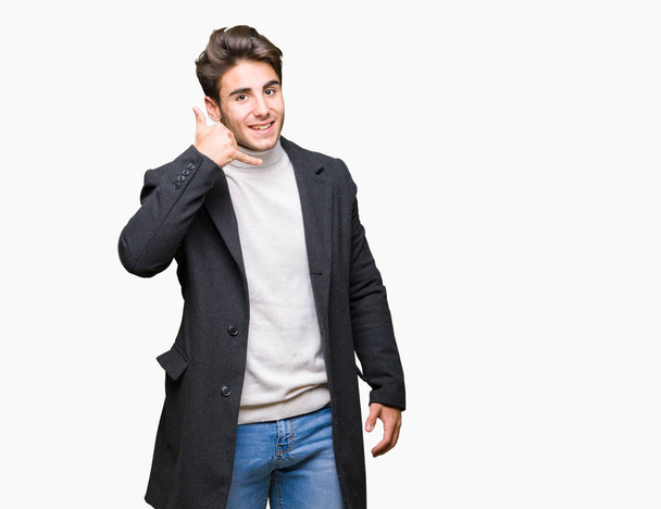 Elegancki młody człowiek sobie płaszcz zimowy na białym tle uśmiechający się robi telefon gest z dłoni i palców, jak rozmawia przez telefon. Komunikacja koncepcje. - Zdjęcie, obraz