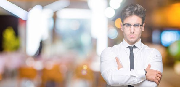 Young business man wearing glasses over isolated background skeptic and nervous, disapproving expression on face with crossed arms. Negative person. - Photo, Image
