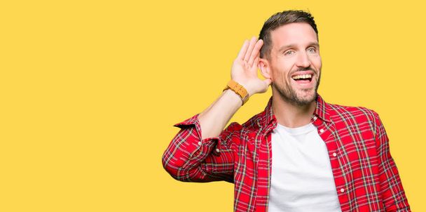 Pohledný muž nosí ležérní košile s úsměvem s rukou přes ucho naslouchá slyšení zvěsti nebo drby. Hluchota koncept. - Fotografie, Obrázek