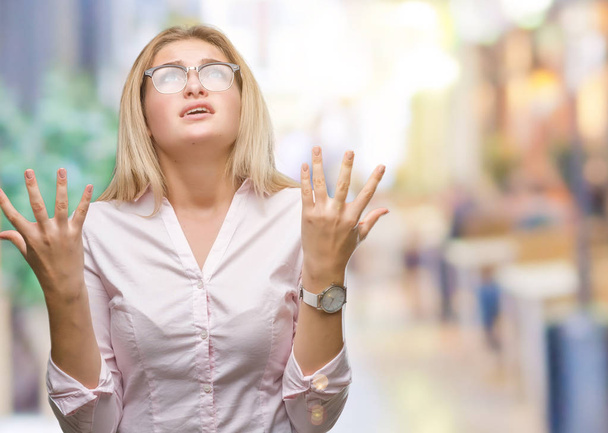Young caucasian business woman wearing glasses over isolated background crazy and mad shouting and yelling with aggressive expression and arms raised. Frustration concept. - Photo, image