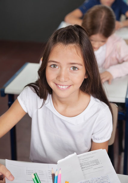 Schoolgirl Sitting At Desk In Classroom - 写真・画像
