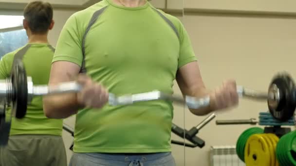 Un uomo in sovrappeso solleva un ez bilanciere mentre si trova in palestra. Esercizio per bicipiti. In forma. Stile di vita sano
. - Filmati, video