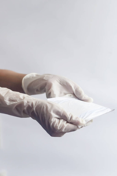 女性の衛生製品。白い背景に生理用ナプキンを持つ医療手袋の女性の手。女性の月経周期を示す期間日の概念. - 写真・画像