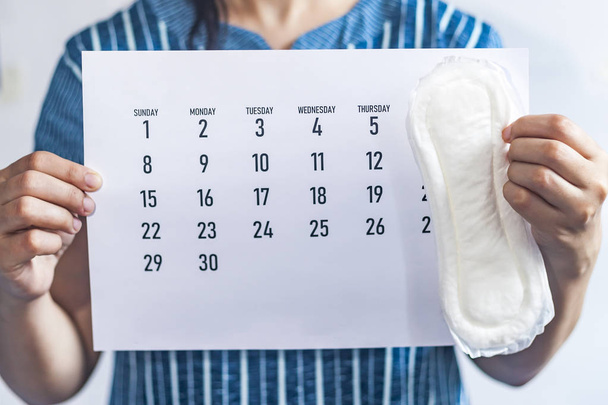Женщина держит месячный календарь и гигиенические прокладки. Календарь менструации. Концепция женского здоровья. Концепция дней периода, показывающая женский менструальный цикл
. - Фото, изображение