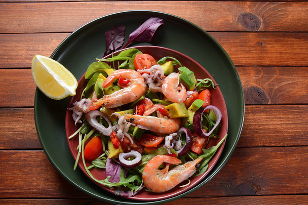 Sea food salad with shrimps, avocado, cherry tomatoes, red hot chilly pepper, red onion, arugula, beet leaves,rukola.balsamic sauce in a plate on a wood background Healthy sea food concept - Foto, Imagem