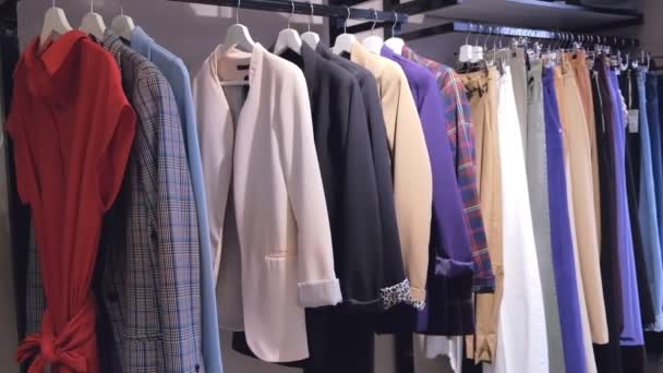 Shooting clothes woman hangers constantly in store indoors. Close up Shot clothing in score, long line with dresses, skirts, coats, sweaters, jackets, pants - Footage, Video