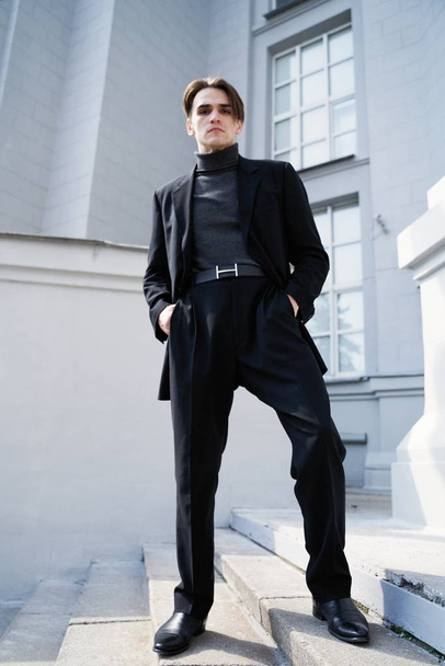 stylischer schöner Mann in schwarzer Kleidung posiert auf der Straße                                 - Foto, Bild