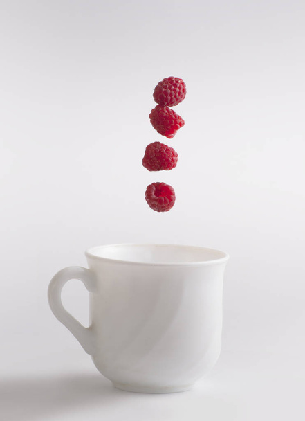 Чашка, в якій падає малиновий, на сірому ізольованому фоні - Фото, зображення